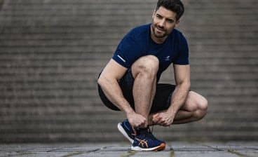 Muž si zavazuje běžecké boty Asics před schodami.