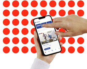 Ruce drží telefon na kterém je načtená Intersport aplikace. V pozadí červené tečky znázorňující věrnostní body.