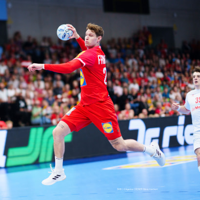 Ein Handballspieler im roten Trikot wirft den Ball im Sprung.