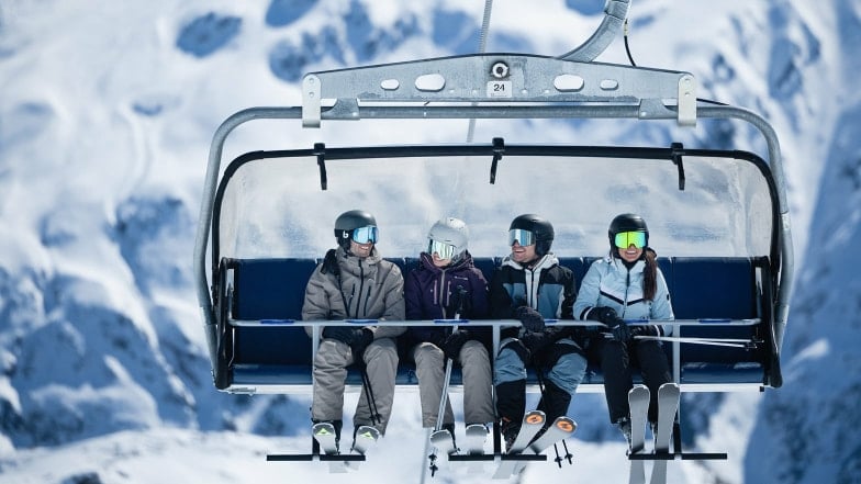 Vier lachende Skifahrer auf einem Sessellift in den verschneiten Bergen.