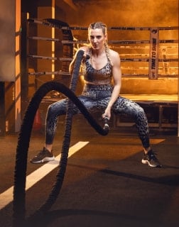 Frau in sportlicher Kleidung führt mit Battle Ropes schnelle Armbewegungen aus. Die Übung verbessert Kraft und Ausdauer.