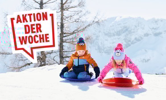 Zwei Kinder fahren mit Plastikbob im Schnee in den Bergen.