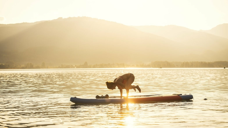 Bei Sonnenuntergang macht diese Frau die Yoga Position Krähe auf dem SUP – was für ein Gleichgewichtssinn!