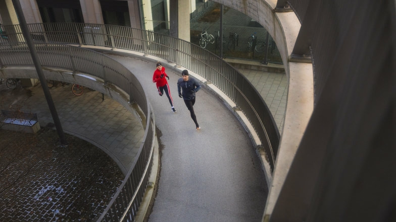 Mann und Frau joggen auf einer geschwungenen Rampe in der Stadt.
