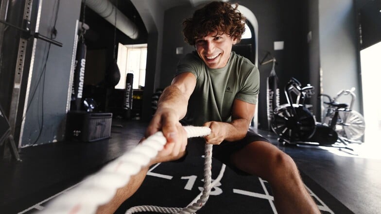 Ein junger Mann zieht an einem Seil im Fitnessstudio.