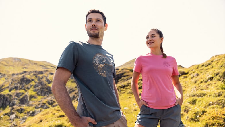 Ein Mann und eine Frau stehen in Funktionsshirts vor einer felsigen Berglandschaft.