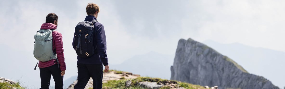 Zwei Personen mit Rucksäcken auf einem Berggrat vor einer markanten Felsformation