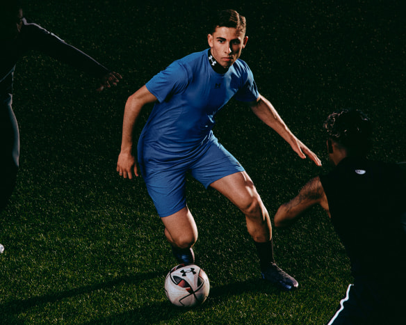 Drei junge Männer spielen abends Fußball in Under Armour Sportkleidung.