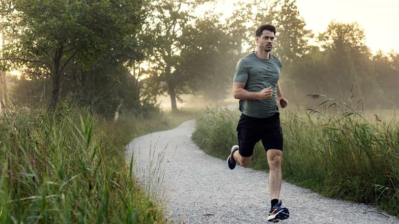 Ein Läufer mit Laufschuhen von Brooks auf einem Schotterweg. Über den Wiesen neben dem Weg hängt noch der Morgennebel.