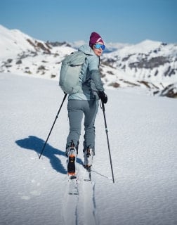 Eine Person mit Rucksack geht auf Skiern und mit Stöcken eine Schneespur bergauf.