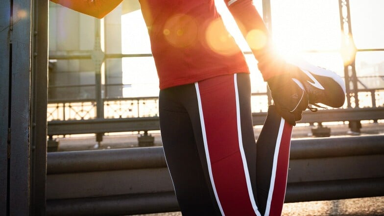 Eine Person in Sportkleidung dehnt sich auf einer Brücke.