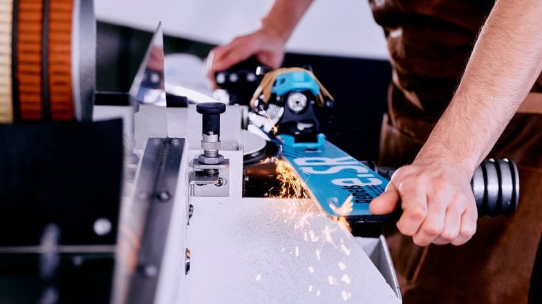 Eine Person schleift die Kanten eines Skis mit einer Maschine.