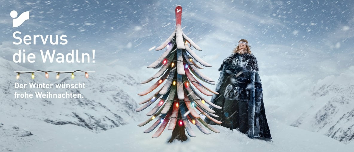 Der Winter wünscht frohe Weihnachten. Er steht neben einem Weihnachtsbaum, der aus Skiern gebastelt wurde.