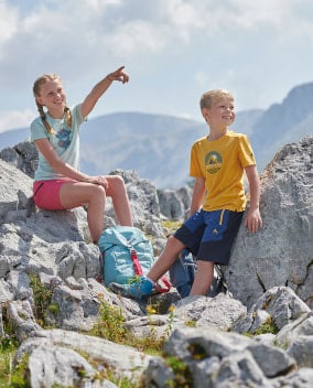 Zwei Kinder machen eine Wanderpause auf Felsen in den Bergen.