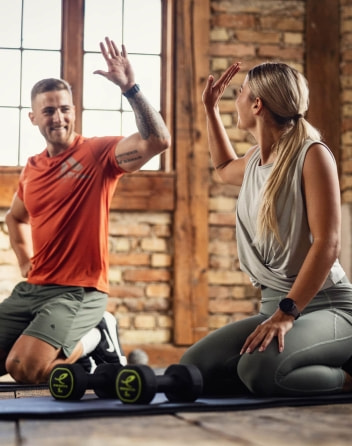 Ein Mann und eine Frau knien auf Trainingsmatten und geben sich nach dem Workout ein High-Five.