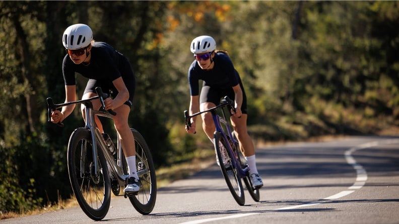 Zwei Rennradfahrer fahren schnell auf einer kurvigen, asphaltierten Straße.