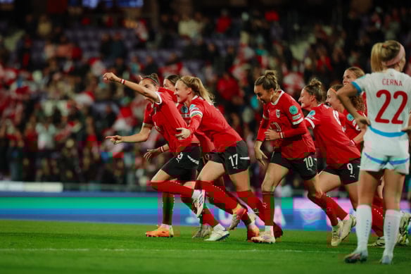 Jubelnde Fußballspielerinnen in roten Trikots feiern auf dem Spielfeld.
