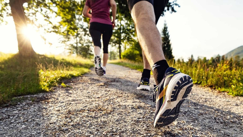 Laufschuhe von Brooks und Asics im Einsatz auf einem Schotterweg im Abendsonnenlicht.