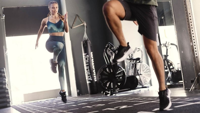 Frau und Mann führen im Fitnessstudio eine Übung mit angehobenen Knien auf einer Trainingsfläche aus.