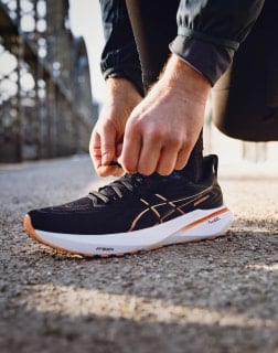 Nahaufnahme einer Person, die auf einem Schotterweg die Schnürsenkel eines schwarzen Laufschuhs bindet.