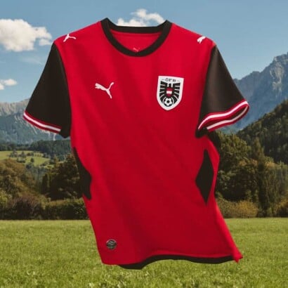 Rotes Fußballtrikot der österreichischen Nationalmannschaft freigestellt vor Berg- und Wiesenlandschaft.