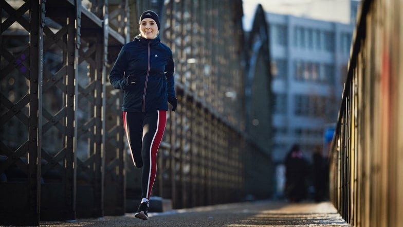 Eine lächelnde Frau joggt im Winter über eine städtische Brücke.