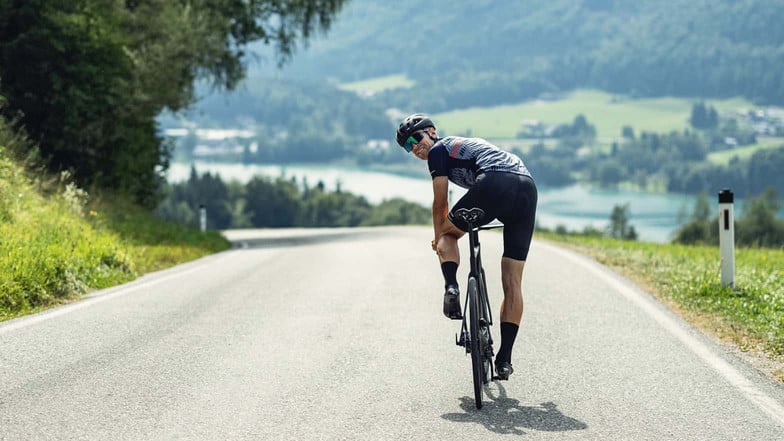 Ein Rennradfahrer schaut auf dem Rennrad über die Schulter, als würde er auf uns warten.