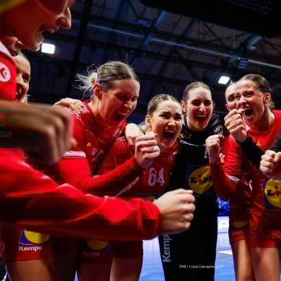 jubelnde Frauen-HandballNationalteam in roten Trikots feiert einen Sieg.