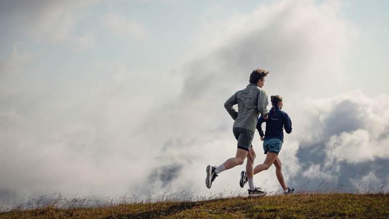 Ein Mann und eine Frau beim Trailrunning – im Hintergrund Wolken am Himmel.