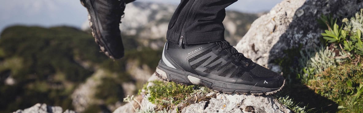 Ein Wanderschuh steht auf felsigem Untergrund in einer Berglandschaft.
