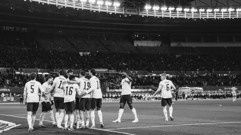 Spieler umarmen sich am Fußballfeld in einem Stadion nach dem Sieg.