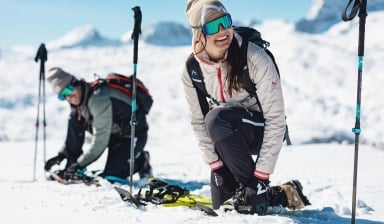 Zwei Personen beim Schneeschuhwandern in einer sonnigen, verschneiten Berglandschaft.