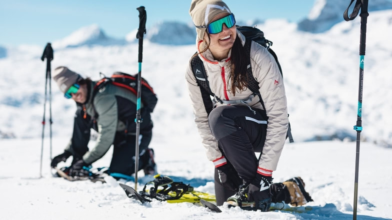 Zwei Personen beim Schneeschuhwandern in einer sonnigen, verschneiten Berglandschaft.