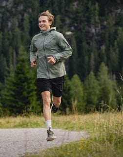 Mann joggt auf einem Schotterweg vor einem Wald mit Bergen im Hintergrund.