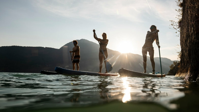 Drei Personen bei Sonnenuntergang am See mit ihren SUPs.