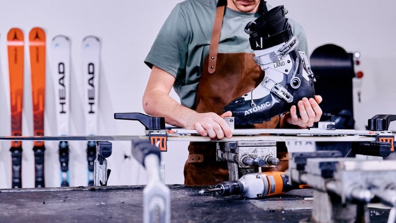 Ein Mann in einer Werkstatt montiert eine Skibindung auf Skiern.