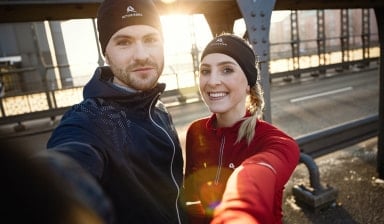 Ein junges Paar in Sportkleidung macht ein Selfie auf einer Brücke.