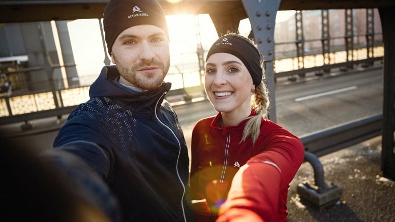 Ein junges Paar in Sportkleidung macht ein Selfie auf einer Brücke.