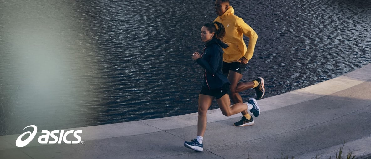 Ein Mann und eine Frau joggen in Sportkleidung am Wasser – mit Asics Gel-Cumulus 28 Laufschuhen.