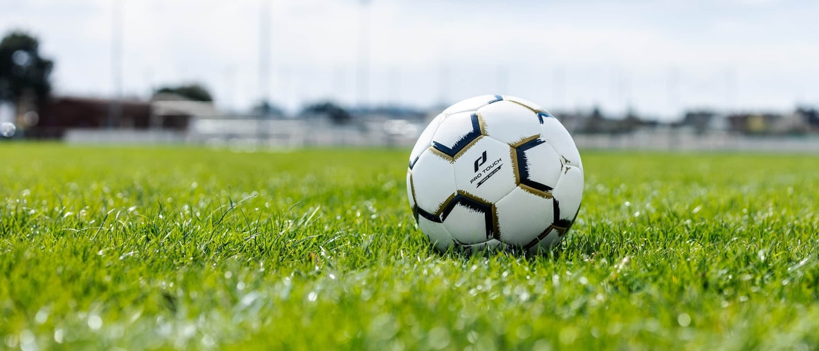 Ein Pro Touch Fußball liegt in der Wiese am Fußballfeld.