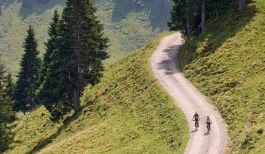Zwei Radfahrer fahren auf einem Schotterweg durch die grünen Berge.