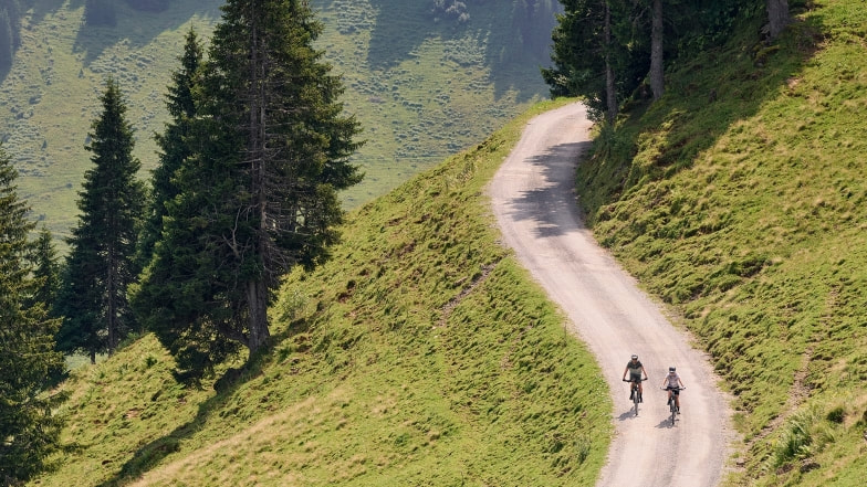 Zwei Radfahrer fahren auf einem Schotterweg durch die grünen Berge.