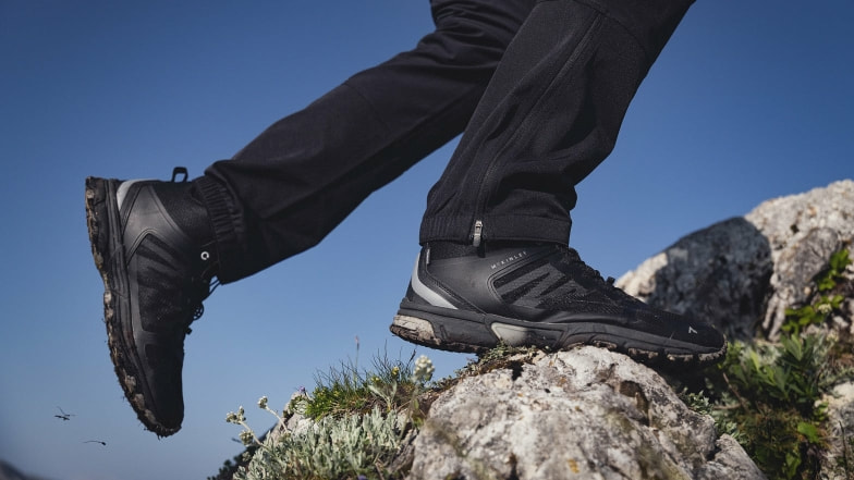 Eine Person mit schwarzen Wanderschuhen wandert auf felsigem Gelände.