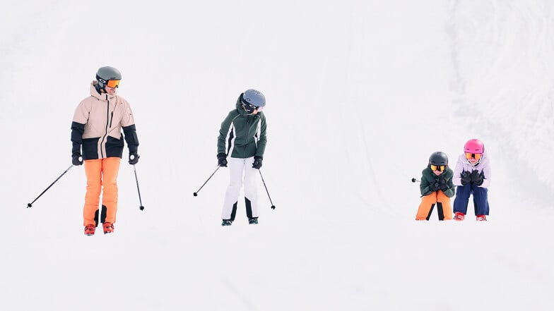 Eltern die mit zwei Kindern die Skipiste runter fahren.