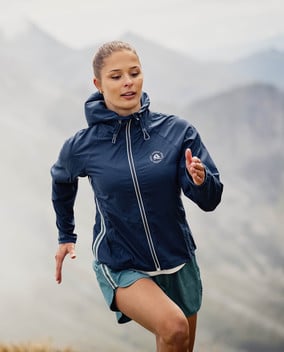 Frau in Sportkleidung läuft in bergiger Landschaft und blickt nach vorne.