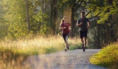 Eine Läuferin und ein Läufer beim gemütlichen Abendlauf. Das Licht der untergehenden Sonne lässt die Wiese neben dem Weg leuchten.