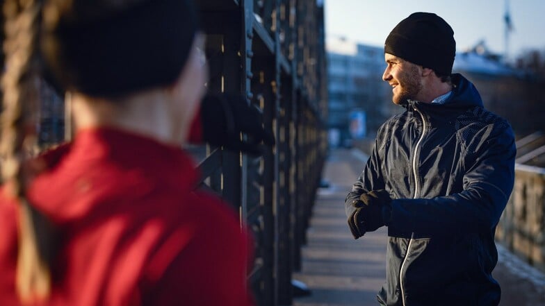 Zwei Läufer in Sportkleidung unterhalten sich auf einer Brücke.