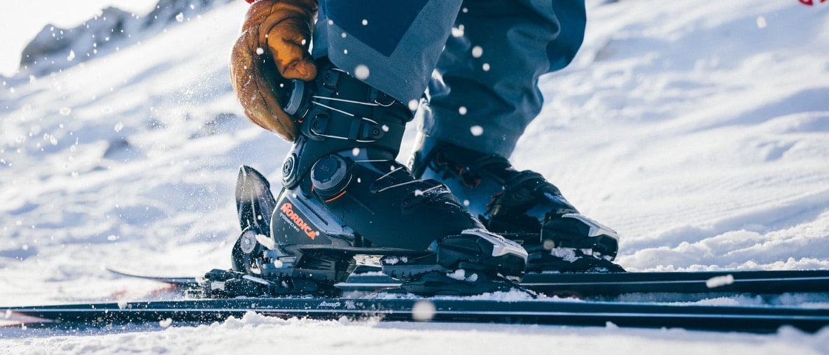 Ein Skifahrer stellt seinen Skischuh mit Handschuhen im Schnee ein.