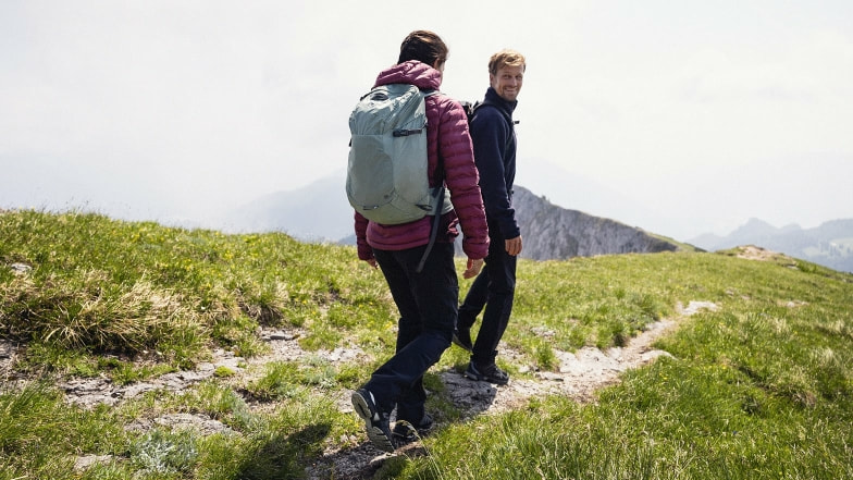 Zwei Personen wandern mit Rucksäcken auf einem Bergpfad.