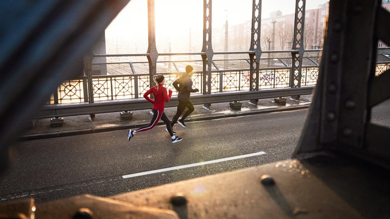 Ein Paar joggt bei Sonnenaufgang über eine Brücke in der Stadt im Winter